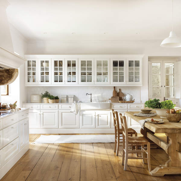 cocina con puertas acrisoladas blancas, suelo de madera natural con muebles blancos, mesa y sillas de madera, plantas aromáticas